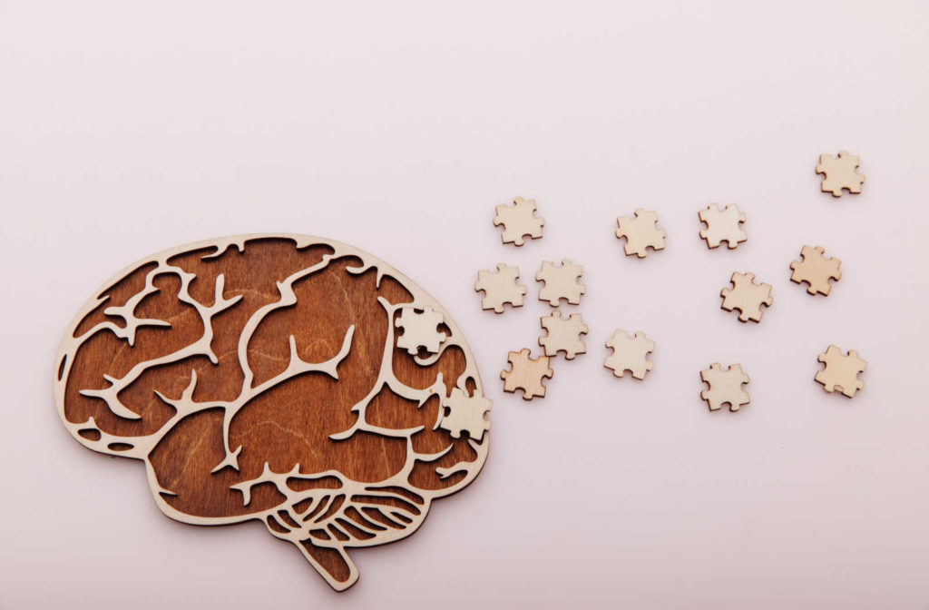 Wood cut out of a brain with puzzle pieces around it.