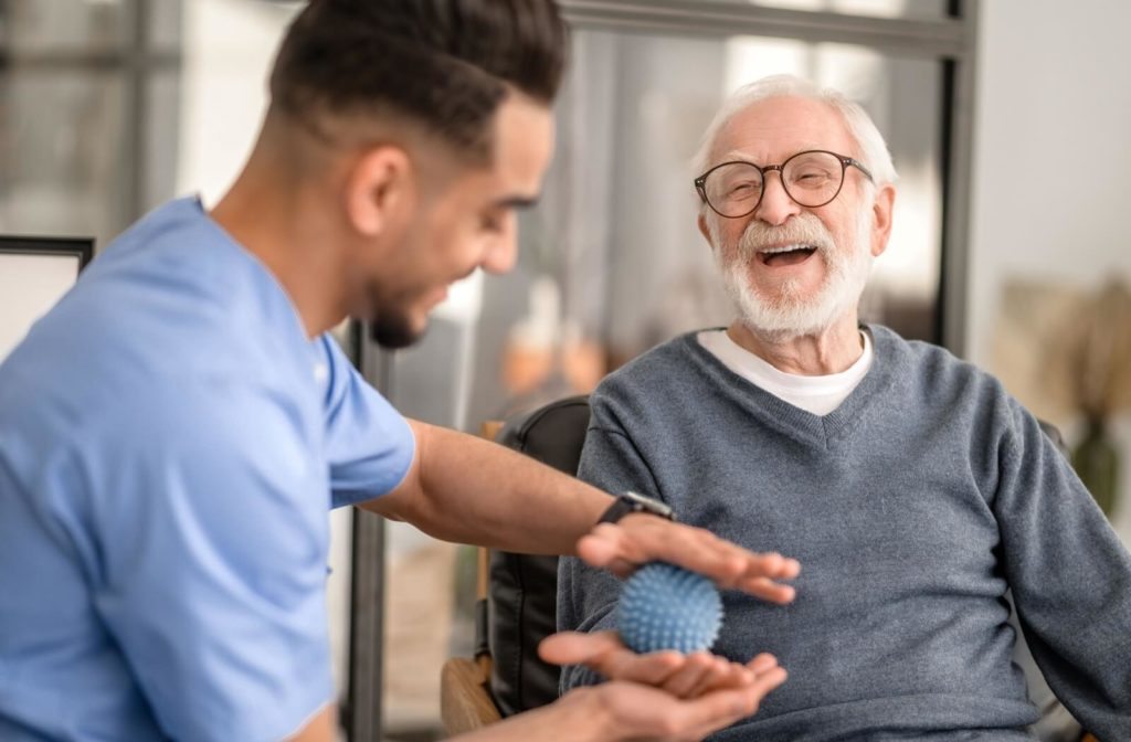 An older adult laughing in senior living while a caregiver uses a small roller ball to massage his hands and manage his chronic pain.