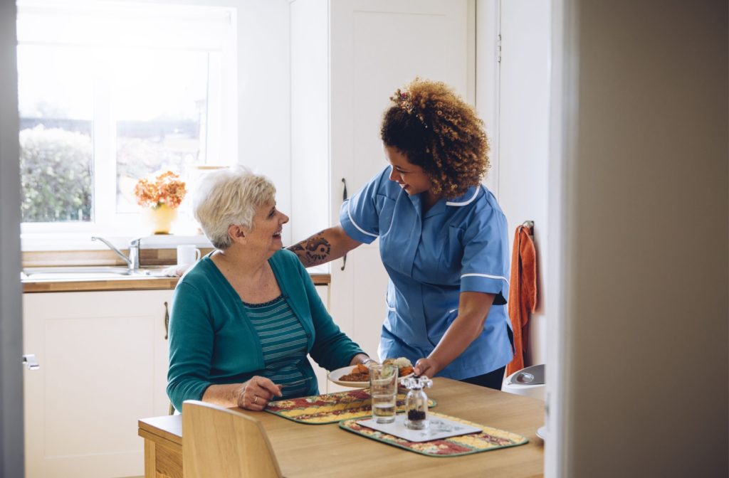 A nurse in an assisted living community brings breakfast to a resident in their room.