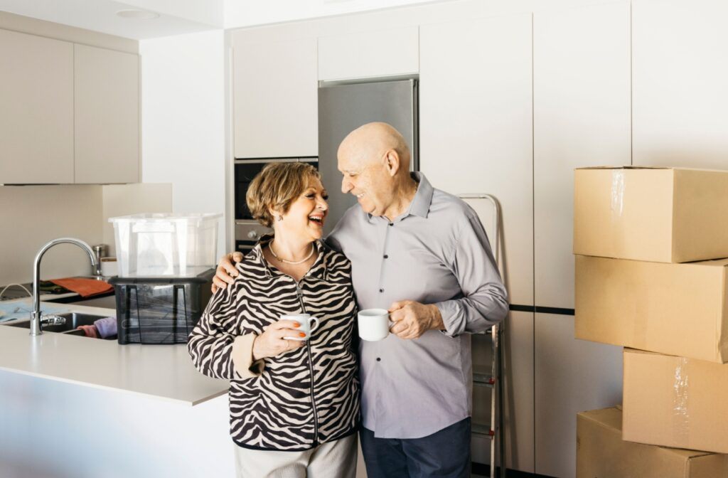 Senior couple smiling and standing together in their packed home, ready to move to an assisted living community.