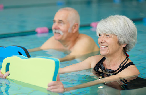 A senior man and woman swim in a pool while holding flotation devices.