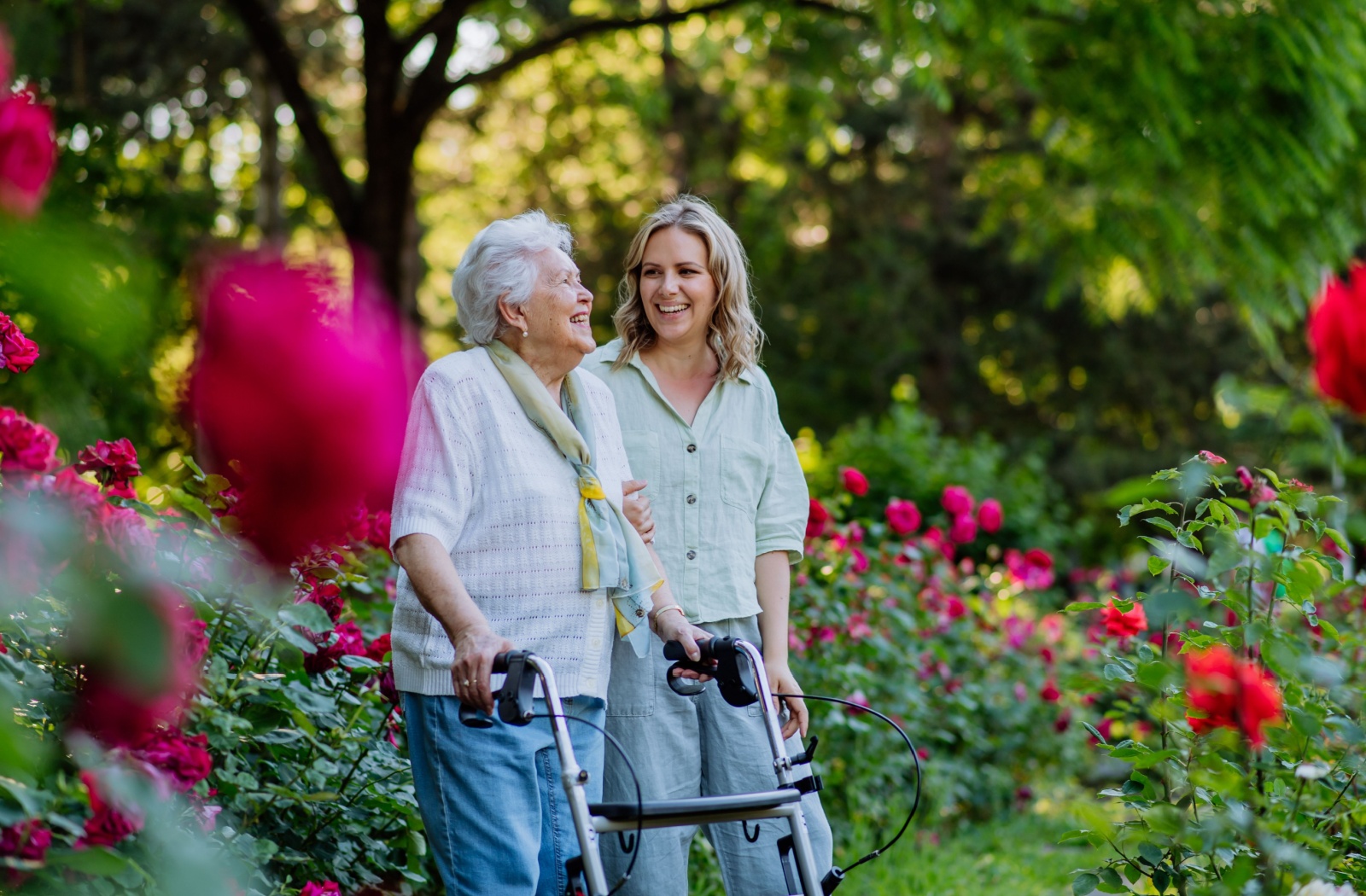 A happy adult child and their parent walking in a garden filled with greenery and flowers.