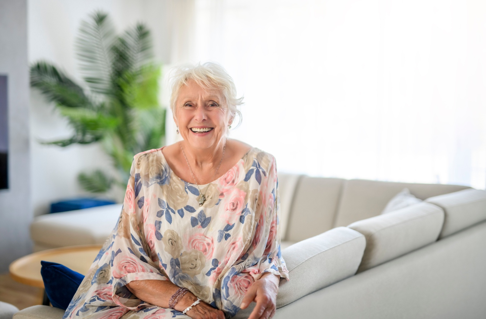 An happy older adult sitting in their living room in assisted living and smiling at the camera.
