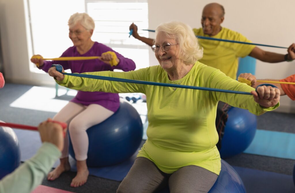 A group of seniors in a wellness class sitting on exercise balls participating in resistance training with bands.