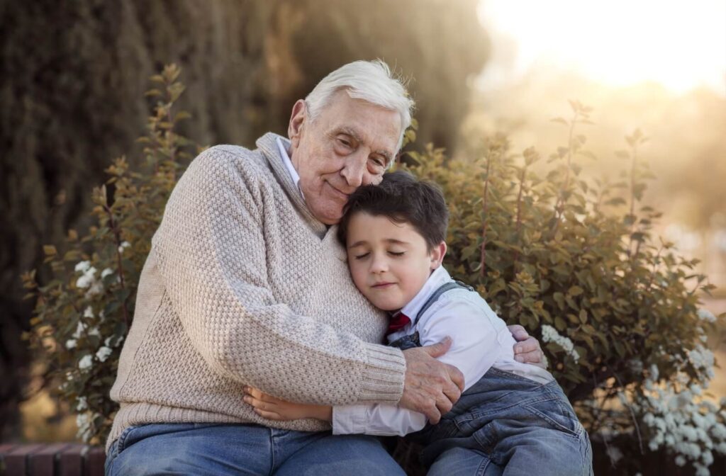  A senior hugs their grandchild while sitting outdoors of their senior living home, expressing gratitude for the visit