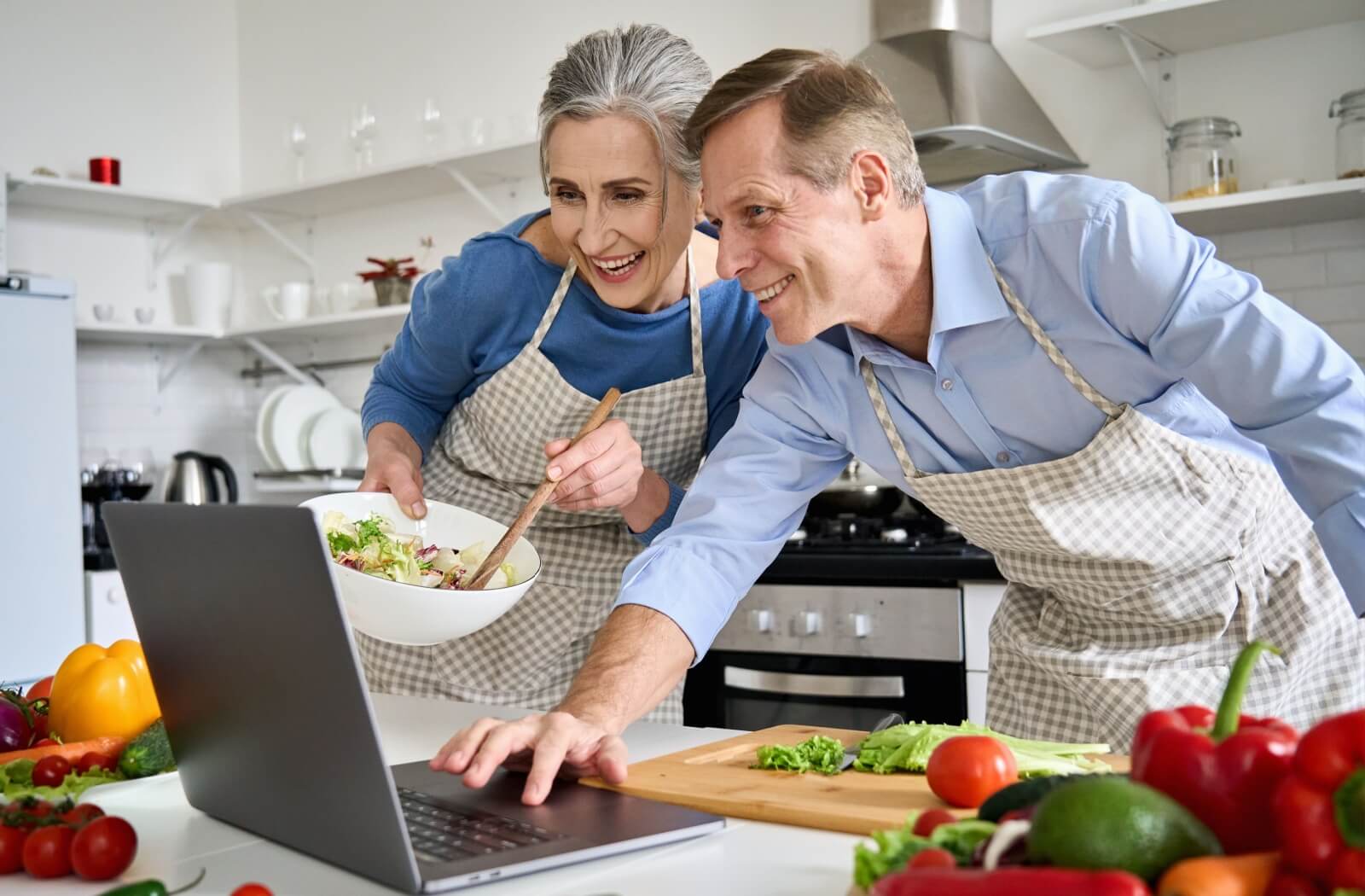 A senior couple use a laptop to follow a dinner recipe that includes nutritious ingredients to support their health